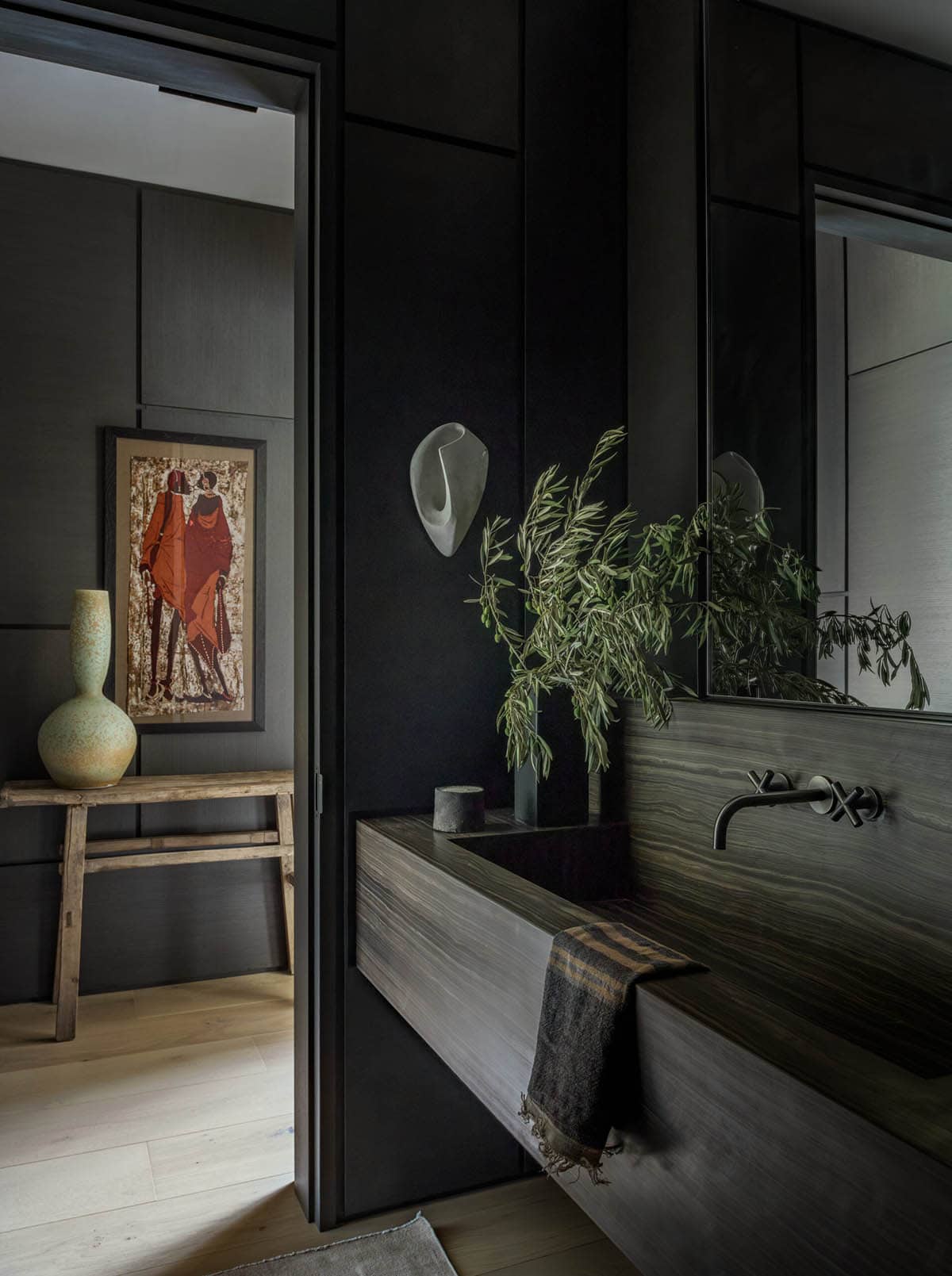 Moody powder room with dark stone trough sink, wall-mount faucet, and olive branch arrangement