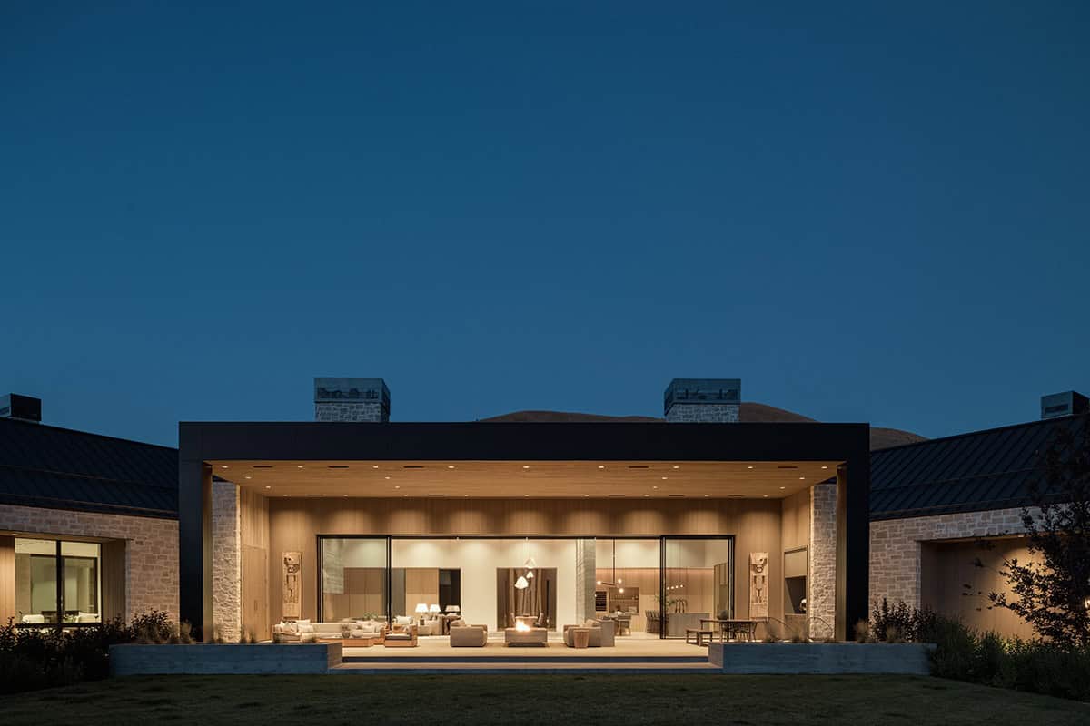 Illuminated covered terrace at night with open sliding doors revealing living and dining areas beyond