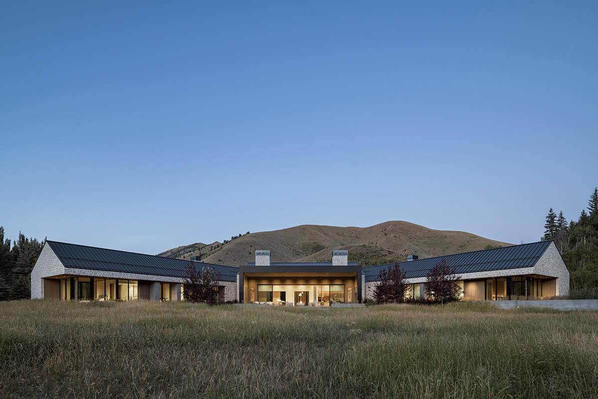 Full rear facade of stone and metal roof estate glowing at dusk against Idaho foothills
