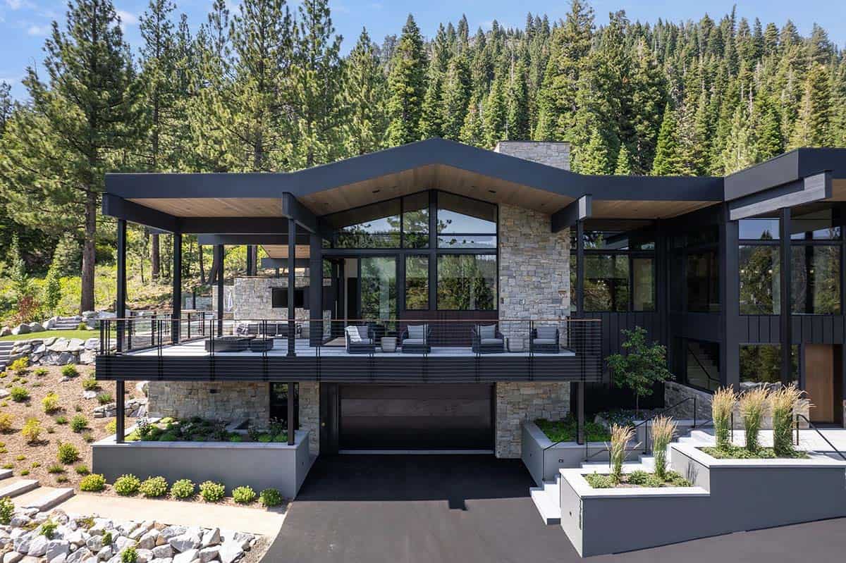 Rear exterior of modern mountain home with dark gabled roof and upper deck