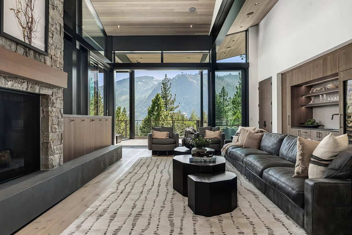 Living room with stone fireplace, leather sofa, and open glass walls framing mountain views