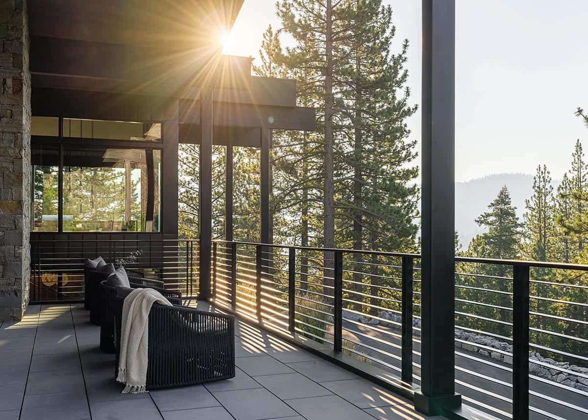 Covered deck at sunset with lounge chairs, steel railings, and pine forest views