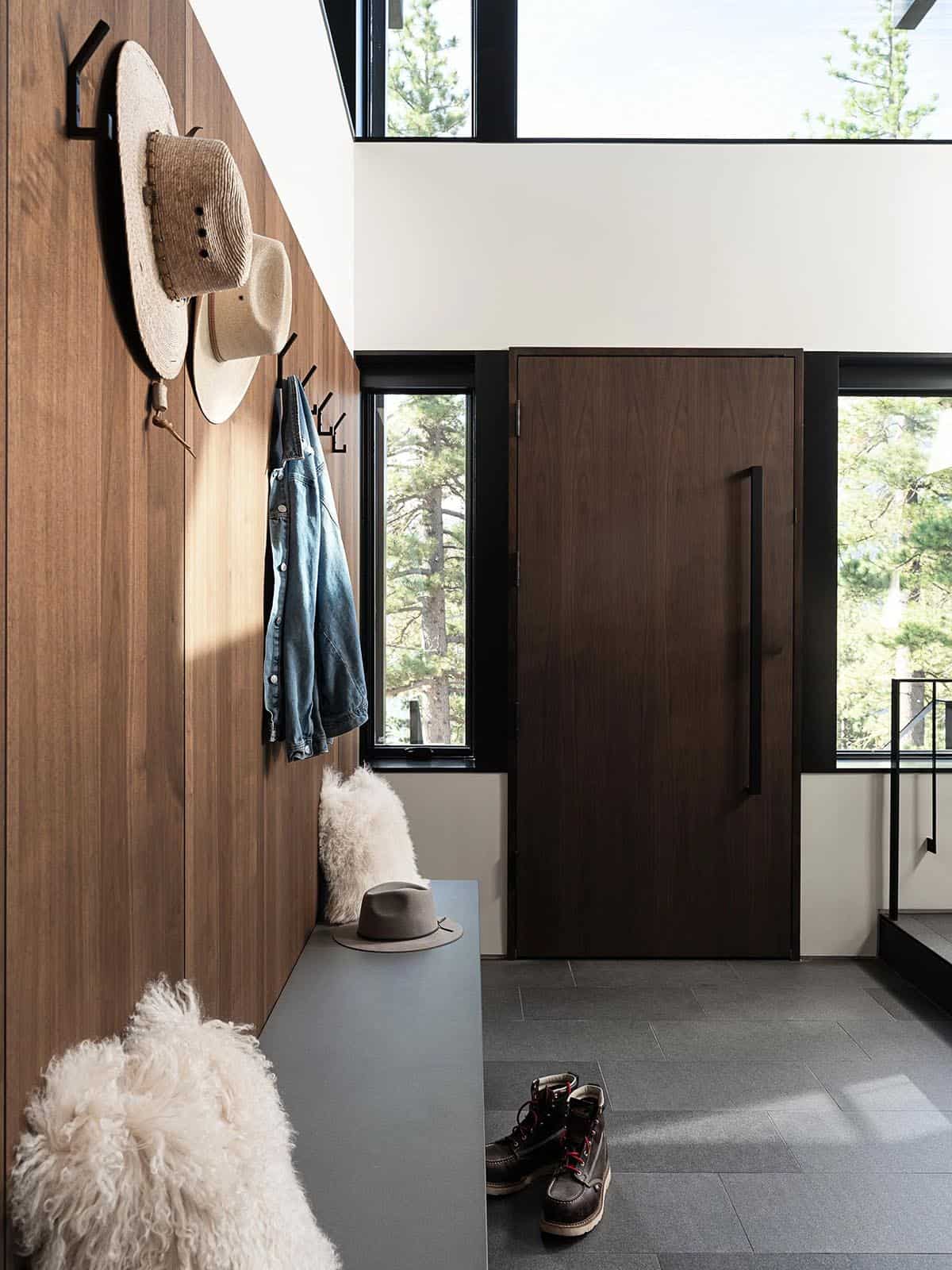 Mudroom entryway with walnut wall panels, black coat hooks, and large wood pivot door