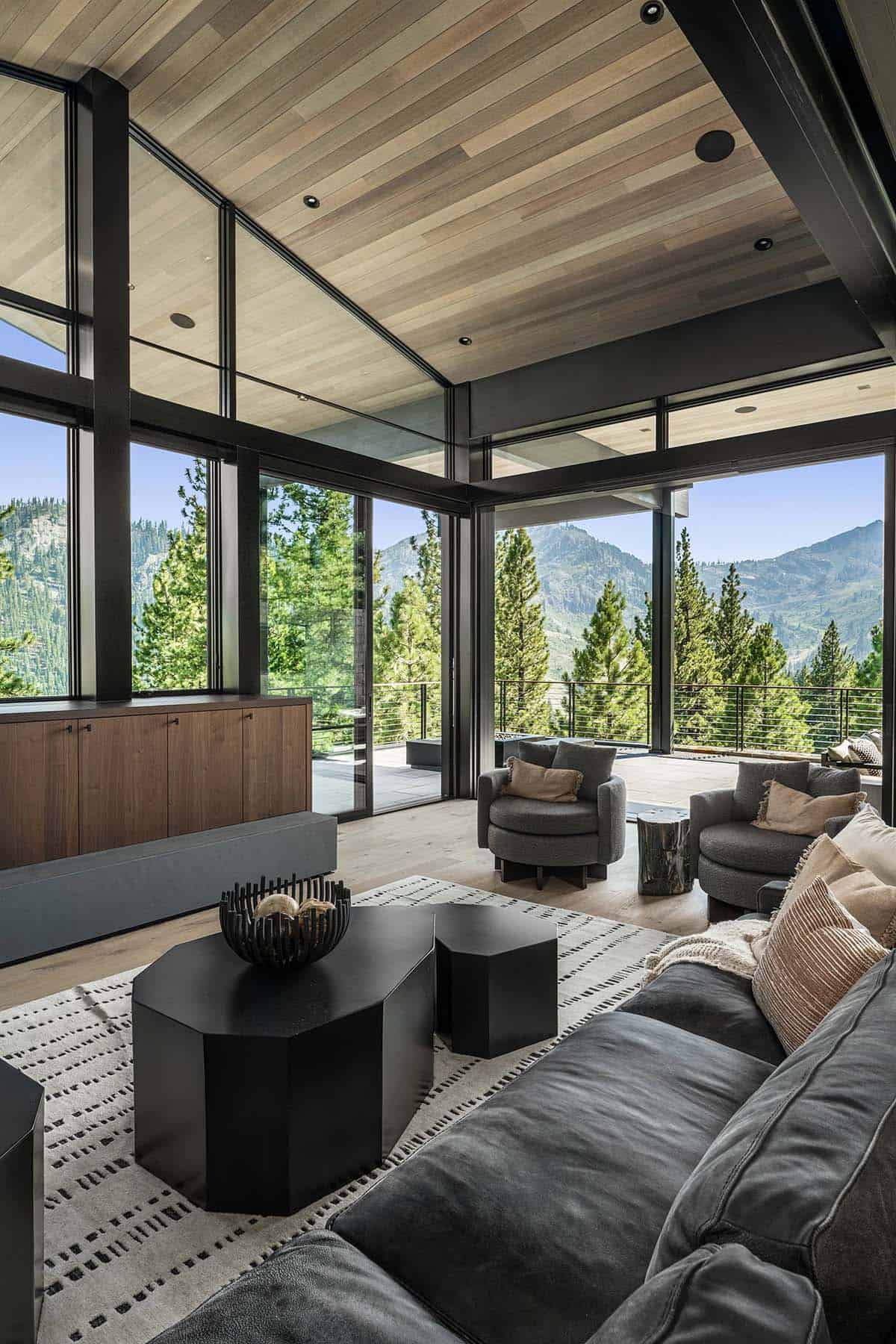 Living room corner with floor-to-ceiling glass walls and panoramic mountain and forest views