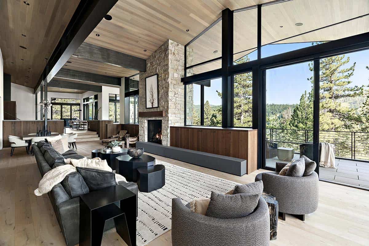 Open-plan great room with stone fireplace, leather sofas, and expansive glass walls