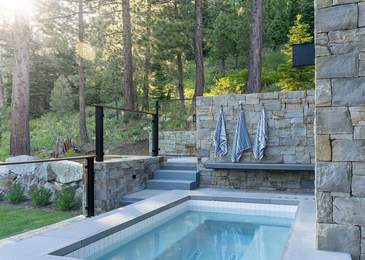 Outdoor plunge pool with stacked stone walls, striped towels, and pine forest setting