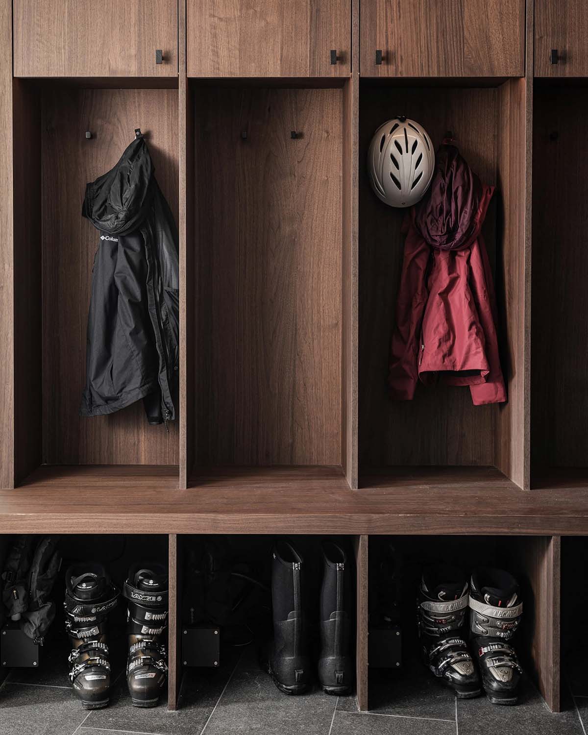Walnut ski locker room with open cubbies, ski boots, helmets, and jackets