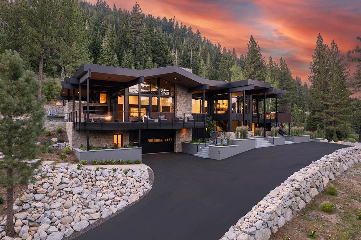 Full front exterior of ski retreat at dusk with warm interior lights and dramatic sunset sky