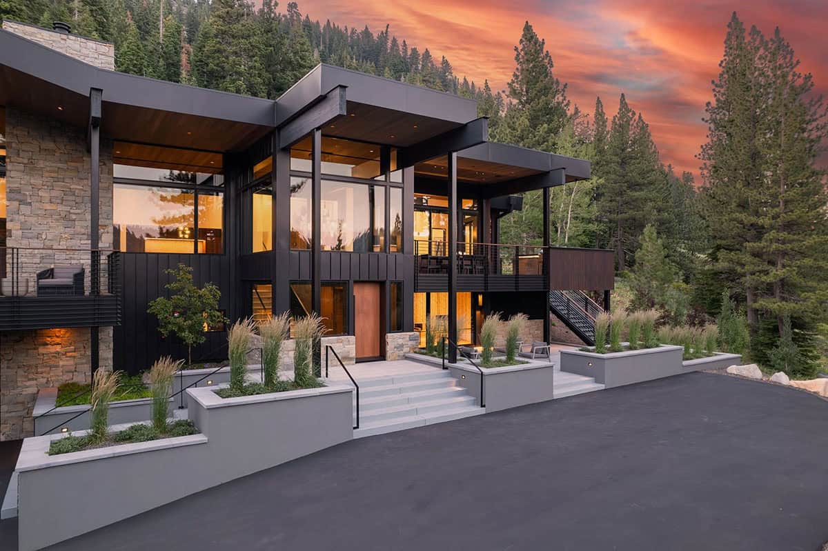Ski retreat entry facade at sunset with warm interior lighting and ornamental grass planters
