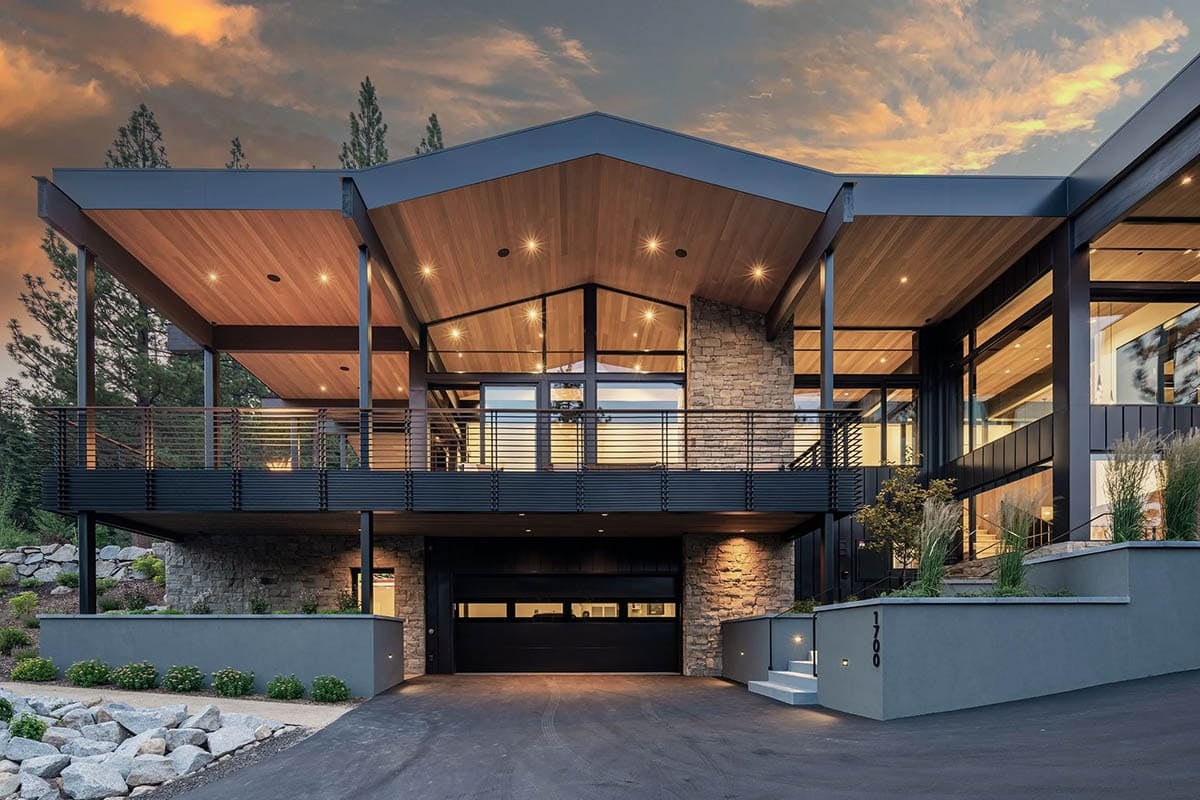 Illuminated garage and covered deck at dusk with wood ceiling and dramatic sunset sky