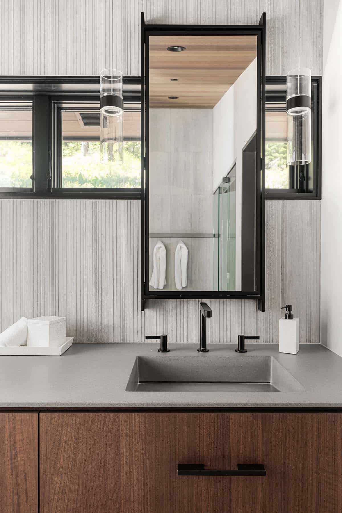 Bathroom vanity with gray stone countertop, black framed mirror, and glass sconce lighting