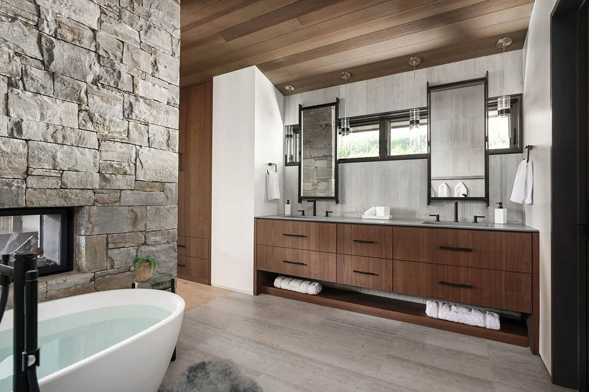Primary bathroom with freestanding soaking tub, stone fireplace wall, and double walnut vanity