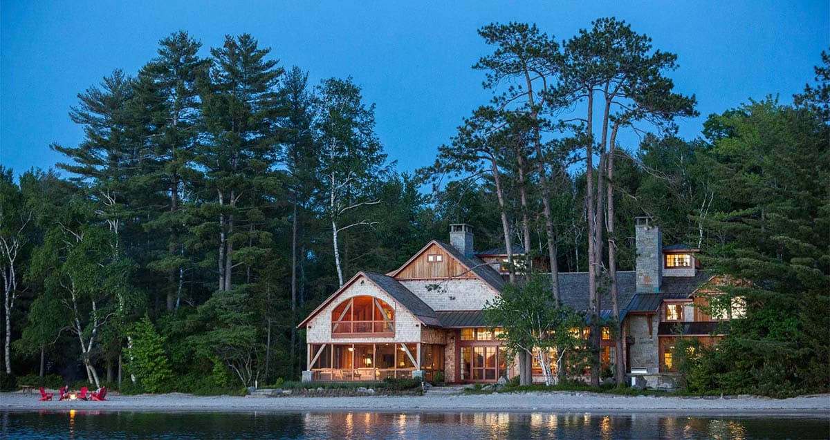 Covered porch detail of the Lake Sunapee New Hampshire shingle-style lake house &mdash; exposed timber rafters, stone piers, and views into the surrounding natural landscape