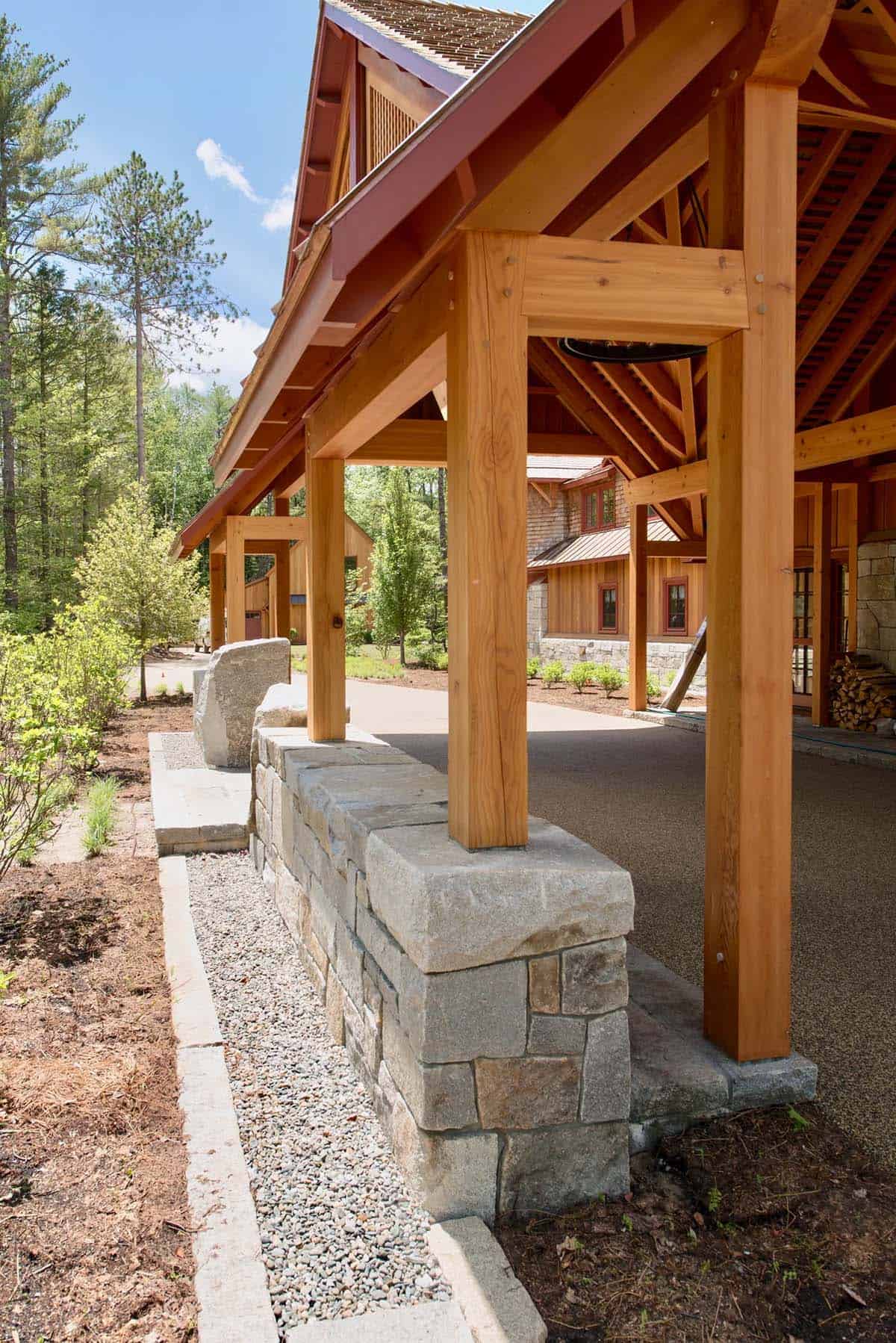 Grand porte-coch&egrave;re entry of the Lake Sunapee New Hampshire lake house &mdash; Douglas fir timber frame construction, granite stone piers, and a statement chandelier visible beneath the covered arrival court