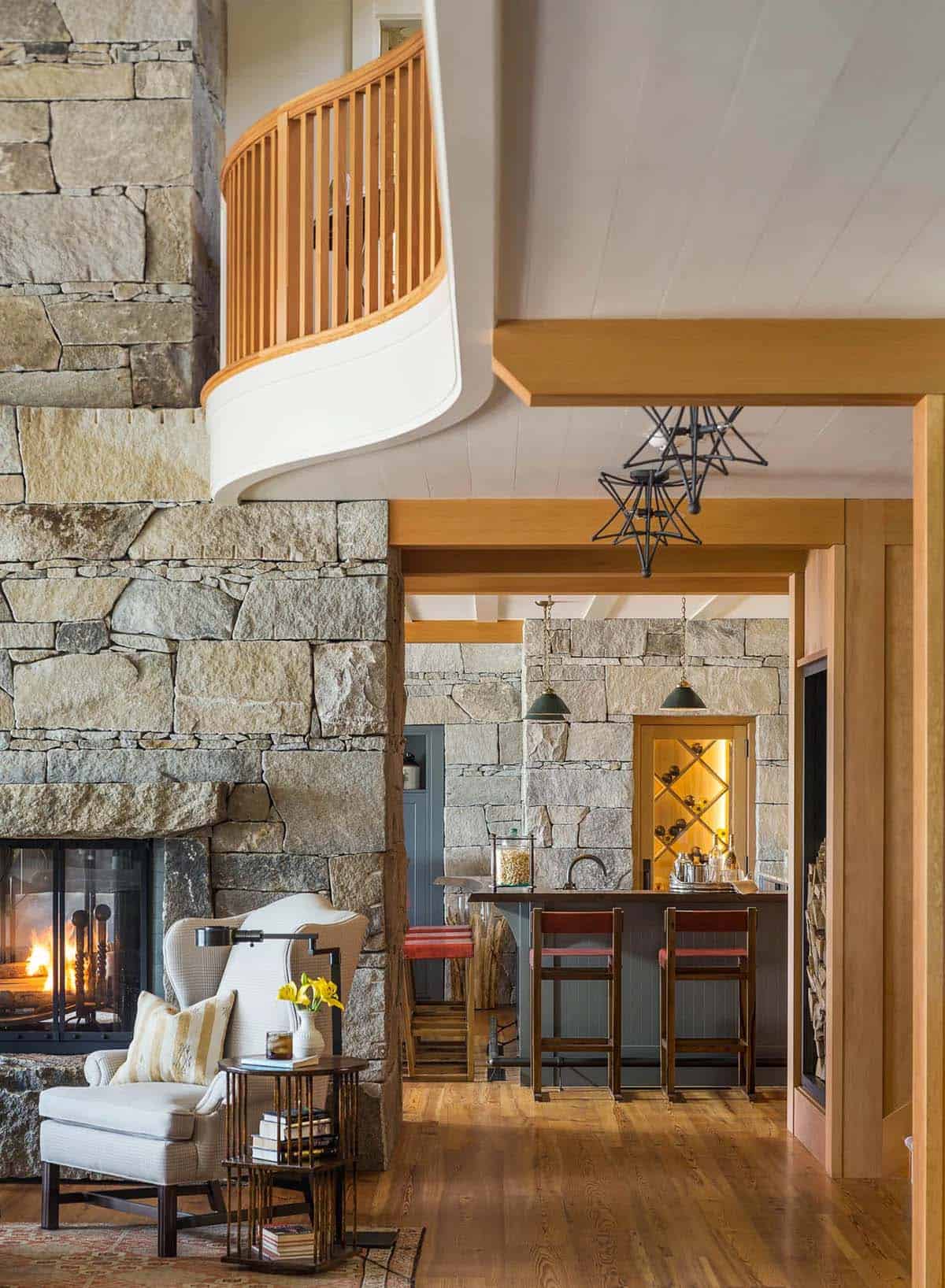 Interior living space of the Lake Sunapee summer house showing traditional furnishings, a stone fireplace wall, generous multi-paned windows, and the warmth of the wood-paneled ceiling and walls