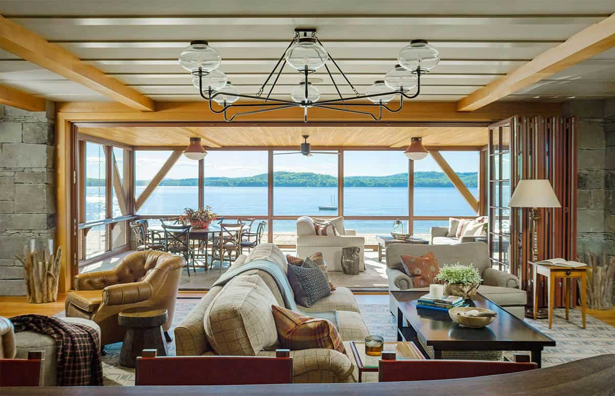 Secondary sitting area inside the Lake Sunapee summer house with natural light from lake-facing windows, traditional upholstered furniture, layered rugs, and warm wood-paneled walls
