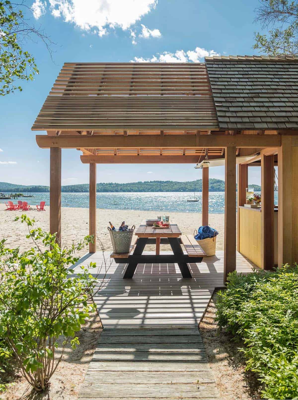 Beachside bar and outdoor entertaining area of the Lake Sunapee New Hampshire lake house property &mdash; a weathered shingle beach cabin with an outdoor bar counter, picnic table, and direct access to the private sandy beach
