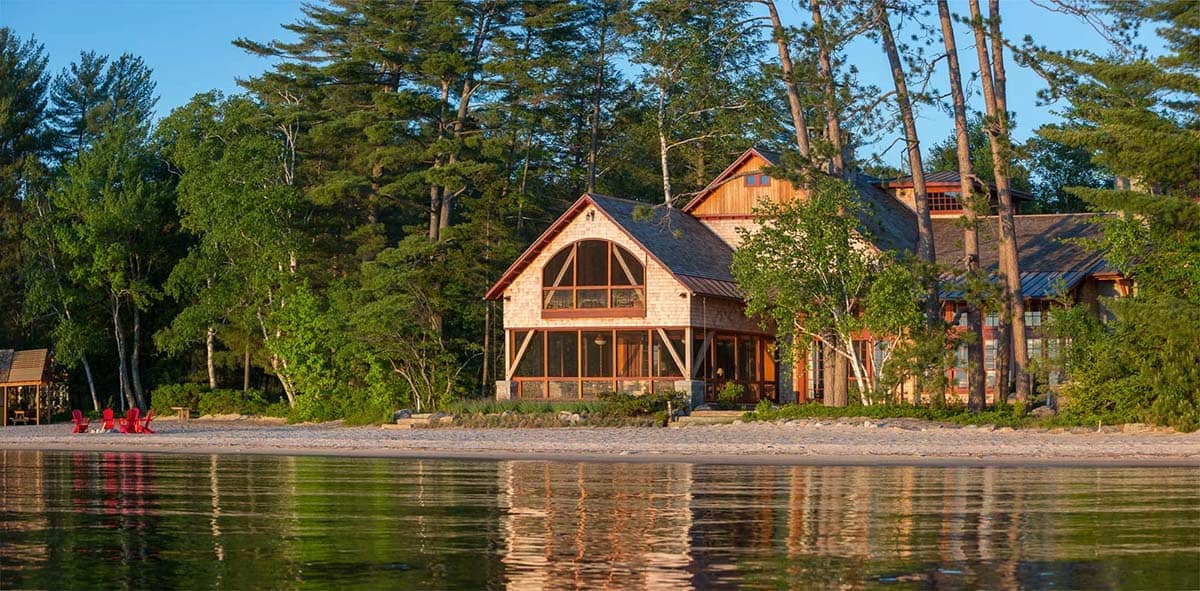 Wide waterfront view from the Lake Sunapee New Hampshire lake house property &mdash; the private sandy beach in the foreground and the open expanse of Lake Sunapee under a clear New England sky