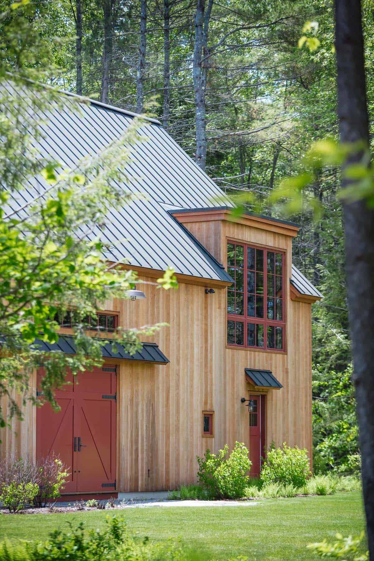 Full exterior view of the classic New England lake house from the waterside &mdash; cedar shingles weathered to silver-gray, multiple roof forms, and the two-acre meadow visible to the side of the property