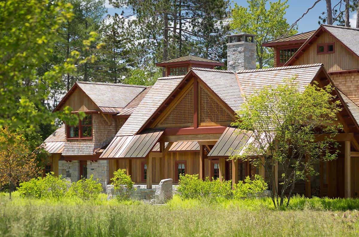Exterior of the New Hampshire lake house with surrounding woodland &mdash; cedar shingles, multiple gabled dormers, and the integration of the home into the mature tree canopy preserved by Pellettieri Associates
