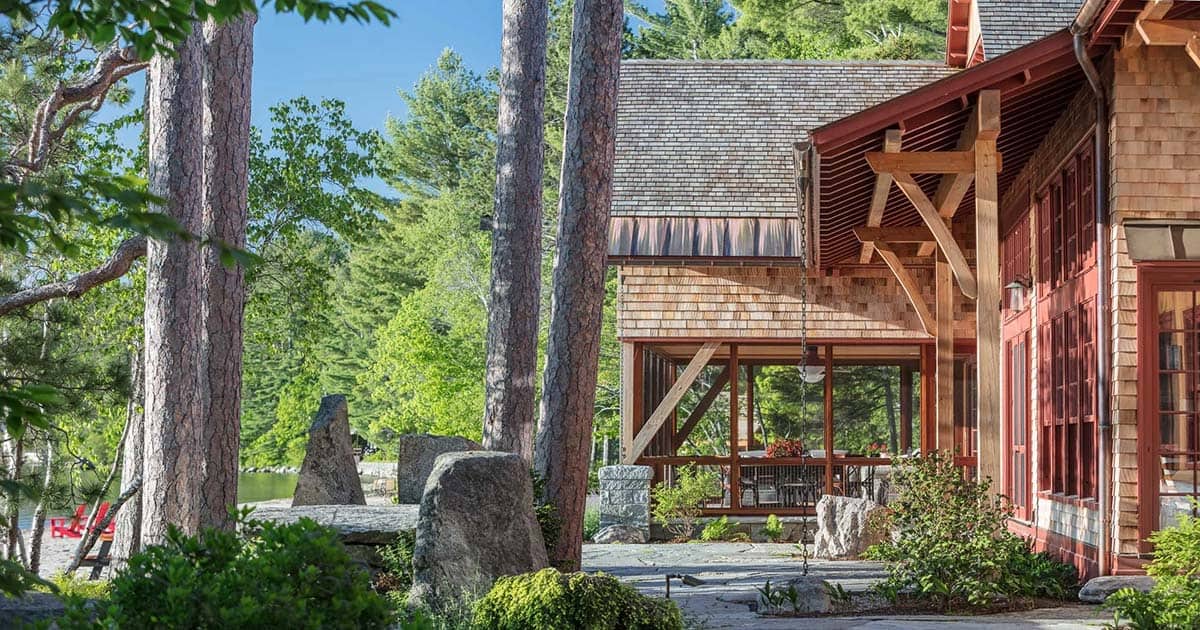 Wide exterior view of the Lake Sunapee summer house and surrounding woodland &mdash; the barn visible to one side and the main house extending along the shoreline, New Hampshire