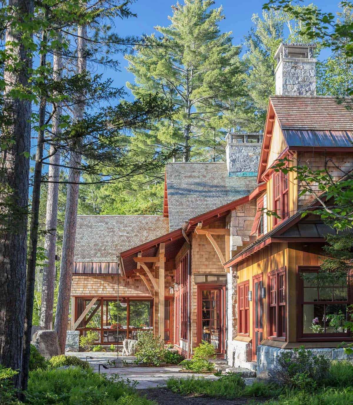 Exterior detail of the Lake Sunapee lake house showing the transition between the main house and the barn structure &mdash; cedar shingles, standing-seam metal roof detail, and native landscape plantings