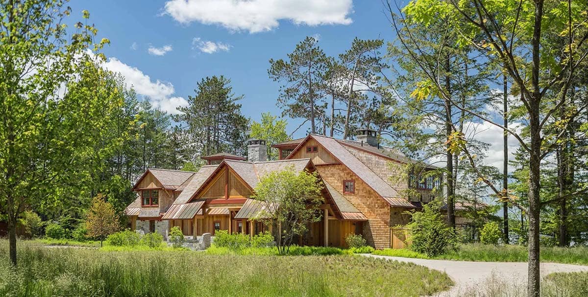Exterior view of the Lake Sunapee New Hampshire summer house from the meadow &mdash; the two-acre meadow created by relocating the private road visible in the foreground, with the shingle-style home beyond
