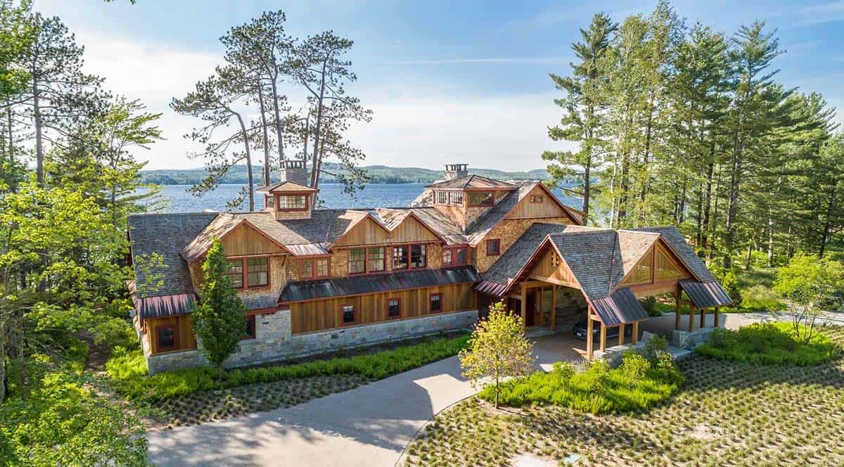 Landscape view of the Lake Sunapee property from the water's edge &mdash; the beach cabin, main house, and barn visible in sequence through the native plantings, showing the full extent of the three-structure compound