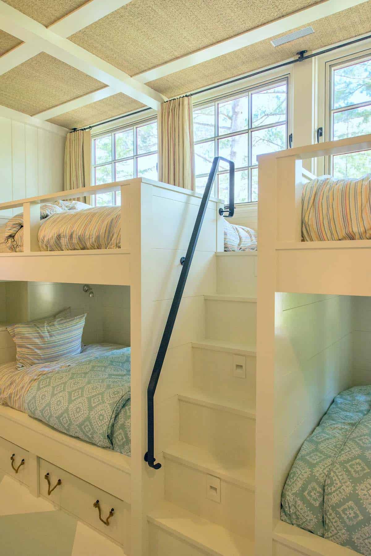 Bunk room detail in the New Hampshire lake house showing the custom built-in bed niches with individual reading lights, storage drawers, and painted wood surround &mdash; designed to sleep multiple children comfortably