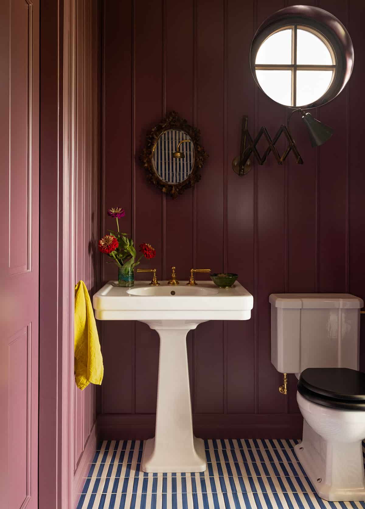 dark plum bathroom with pedestal sink, round porthole window, and striped tile floor, Colorado equestrian home