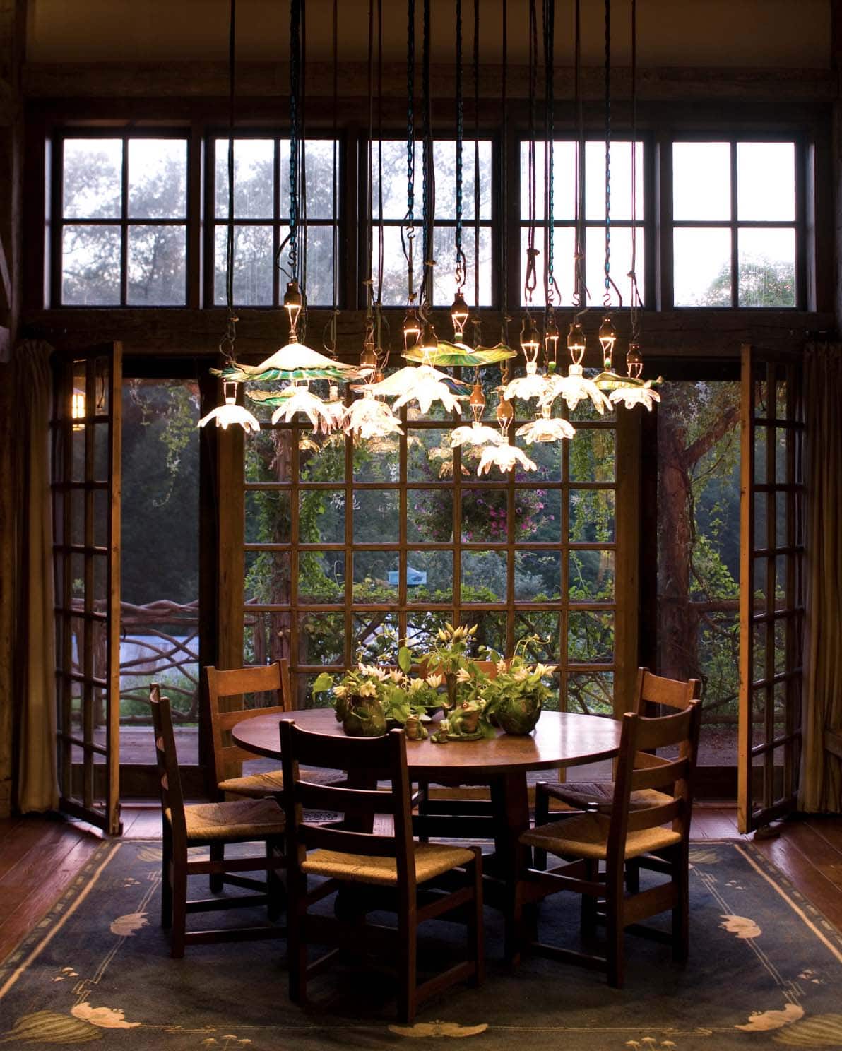 Round dining table beneath cascading daisy chandelier with French doors and garden views