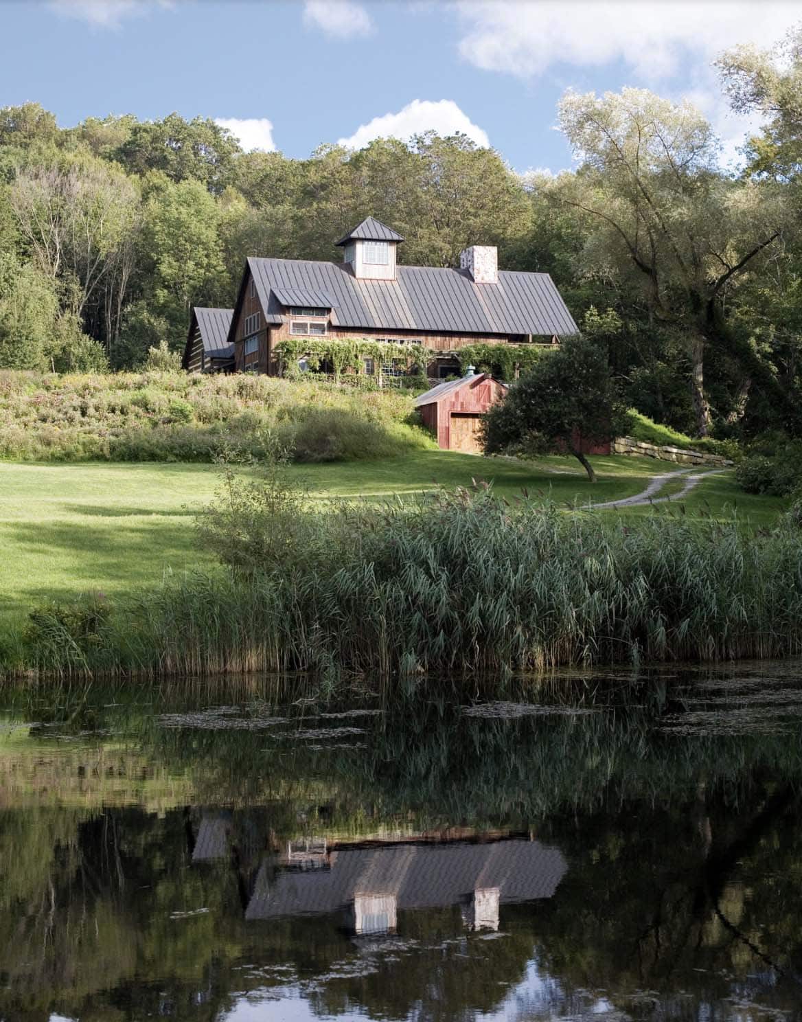 Log cabin retreat reflected in pond with red barn outbuilding and lush hillside setting