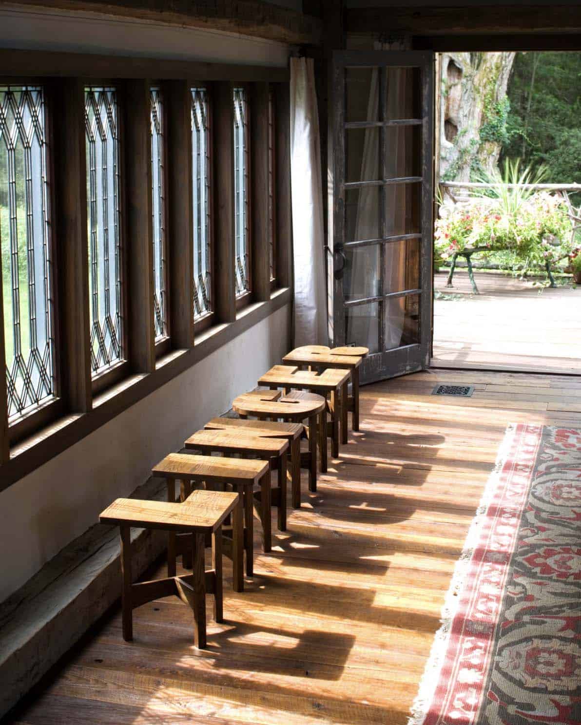 Sunlit screened porch with leaded glass windows, row of wood stools, and garden door