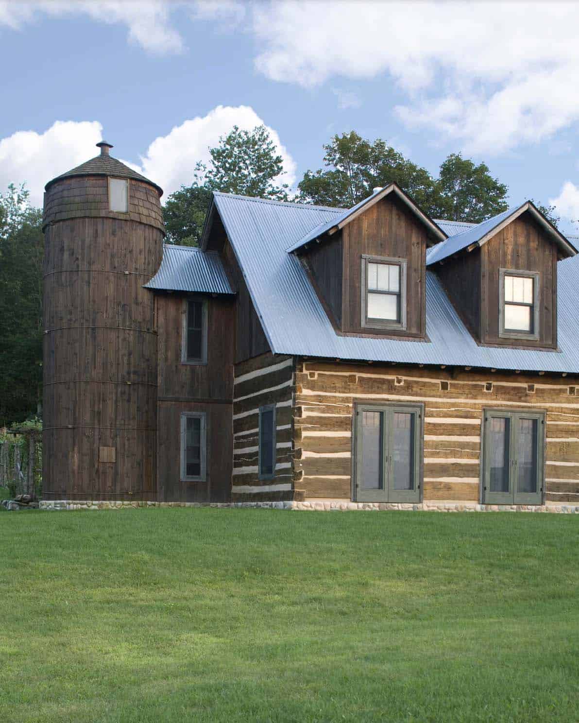 Log cabin exterior with dormer windows, metal roof, and wooden silo outbuilding