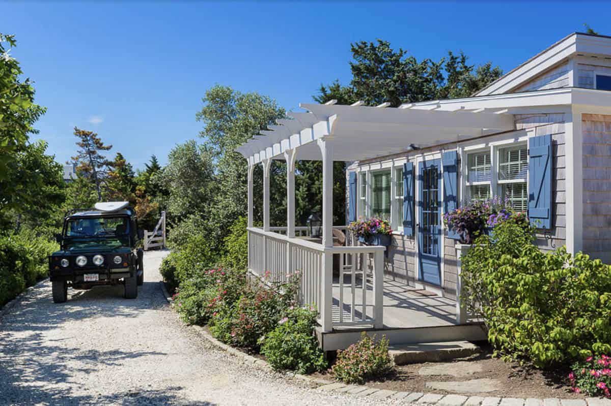 Cedar shingle beach cottage with white pergola, blue shutters, and flower-filled window boxes