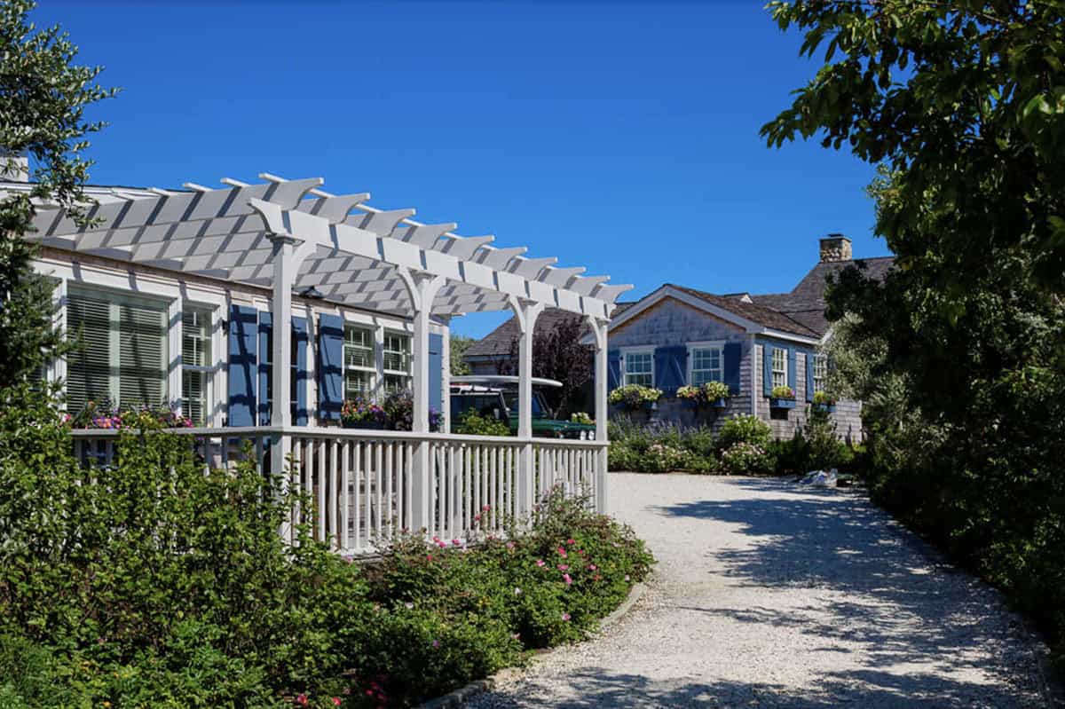 White pergola and cedar shingle cottages connected by gravel driveway with cottage gardens