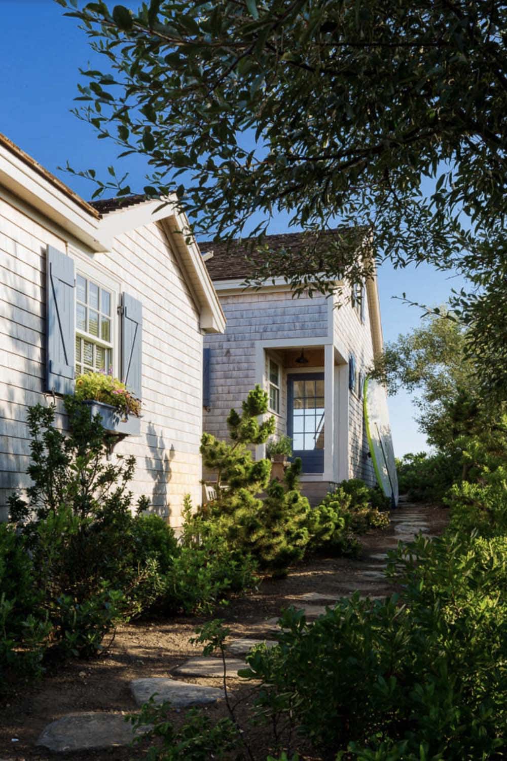 Stone pathway leading to blue front door of cedar shingle beach cottage surrounded by lush plantings
