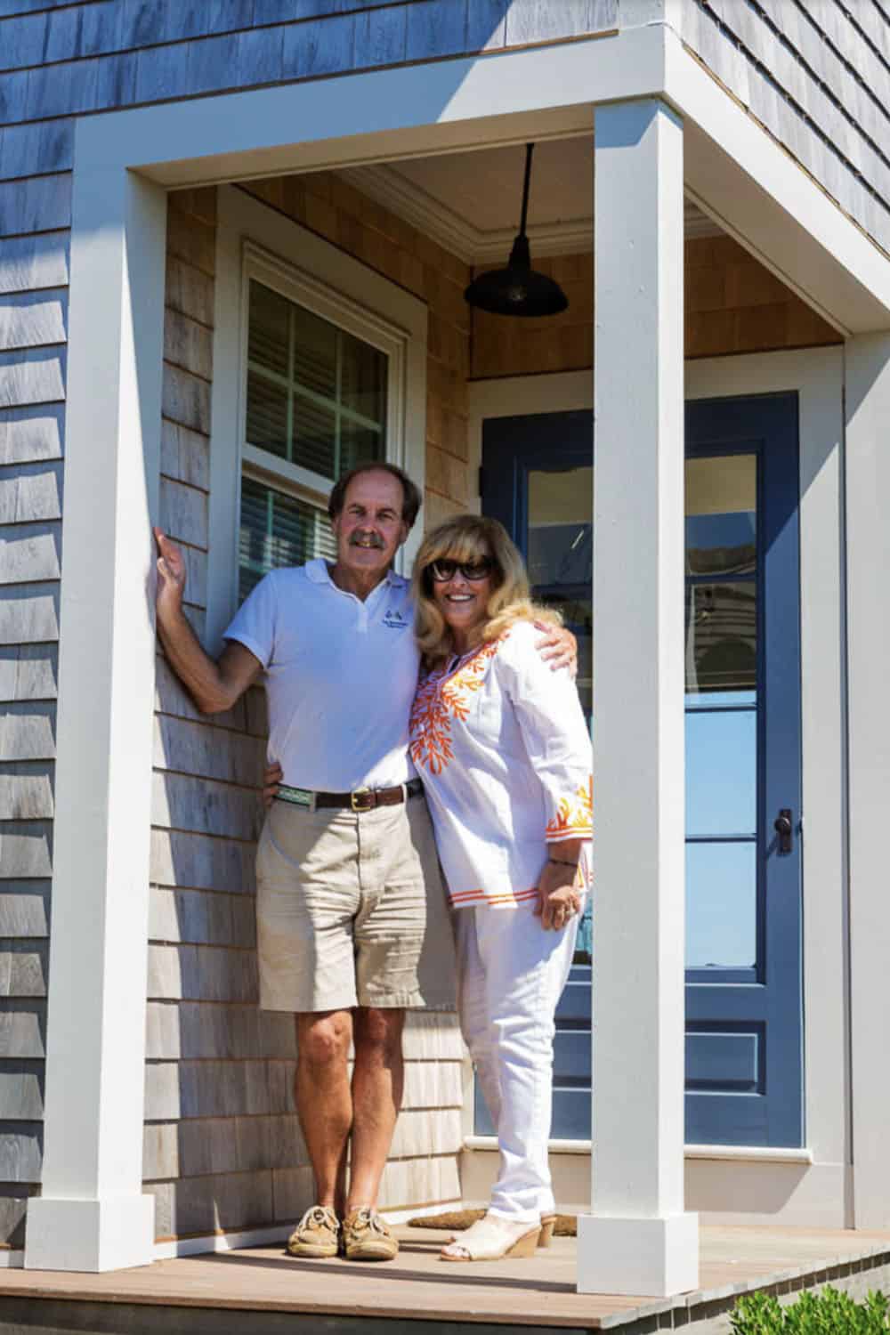 Couple standing at blue front door of cedar shingle beach cottage with barn pendant light