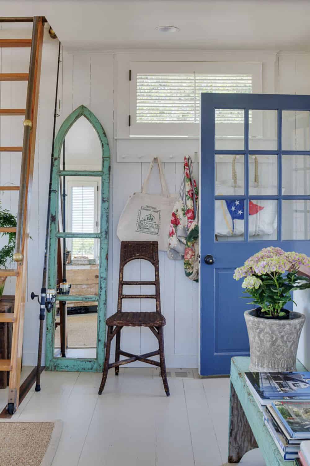 Cottage entryway with blue Dutch door, arched mirror, wicker chair, and fishing rods