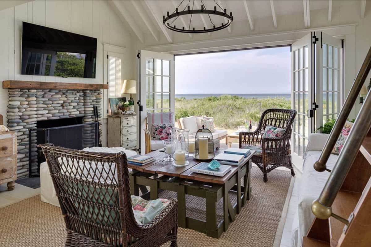 Living room with stacked river rock fireplace, wicker chairs, floral cushions, and ocean views