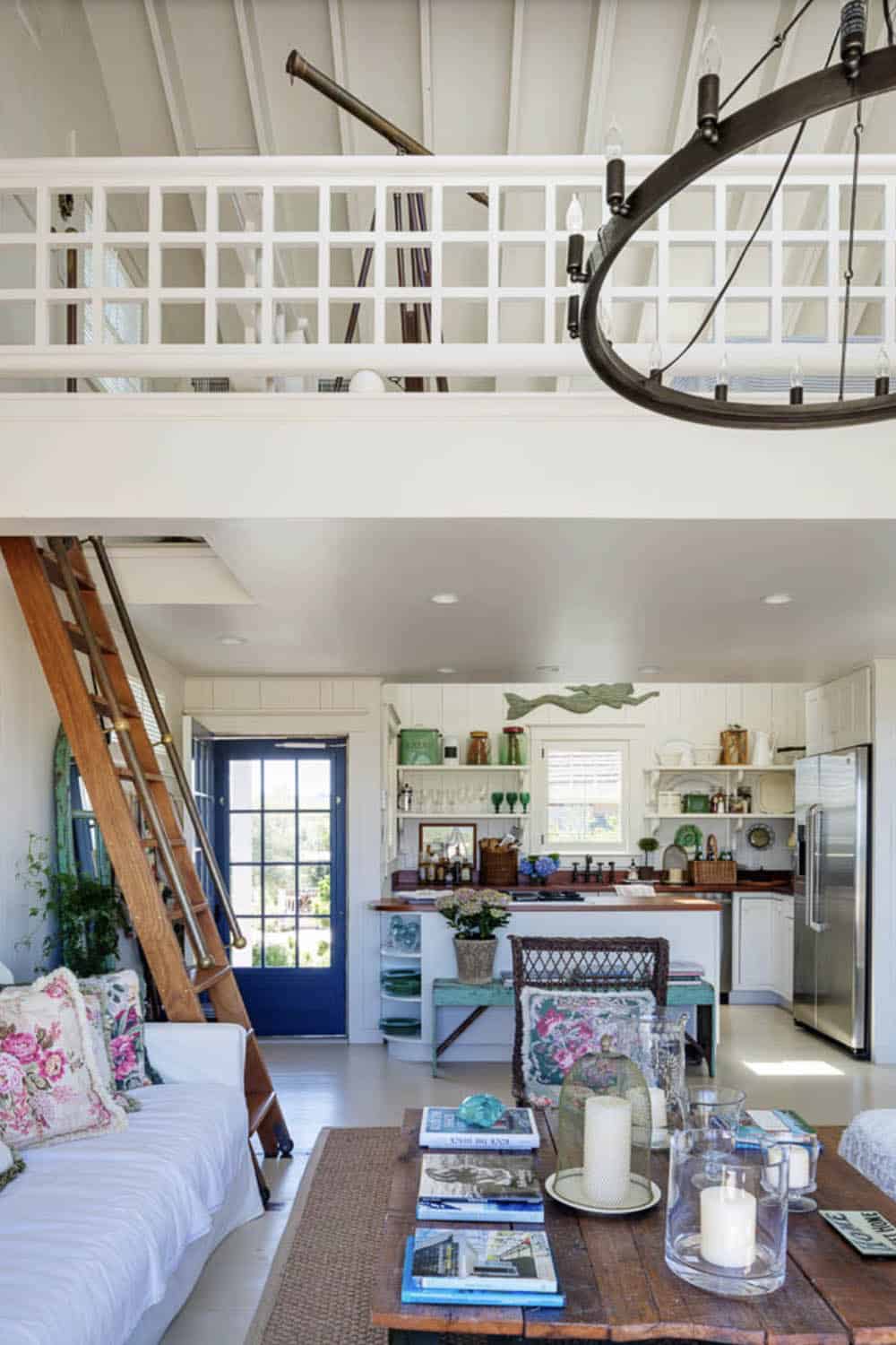 Open-plan living area with loft above, library ladder, white kitchen, and blue front door