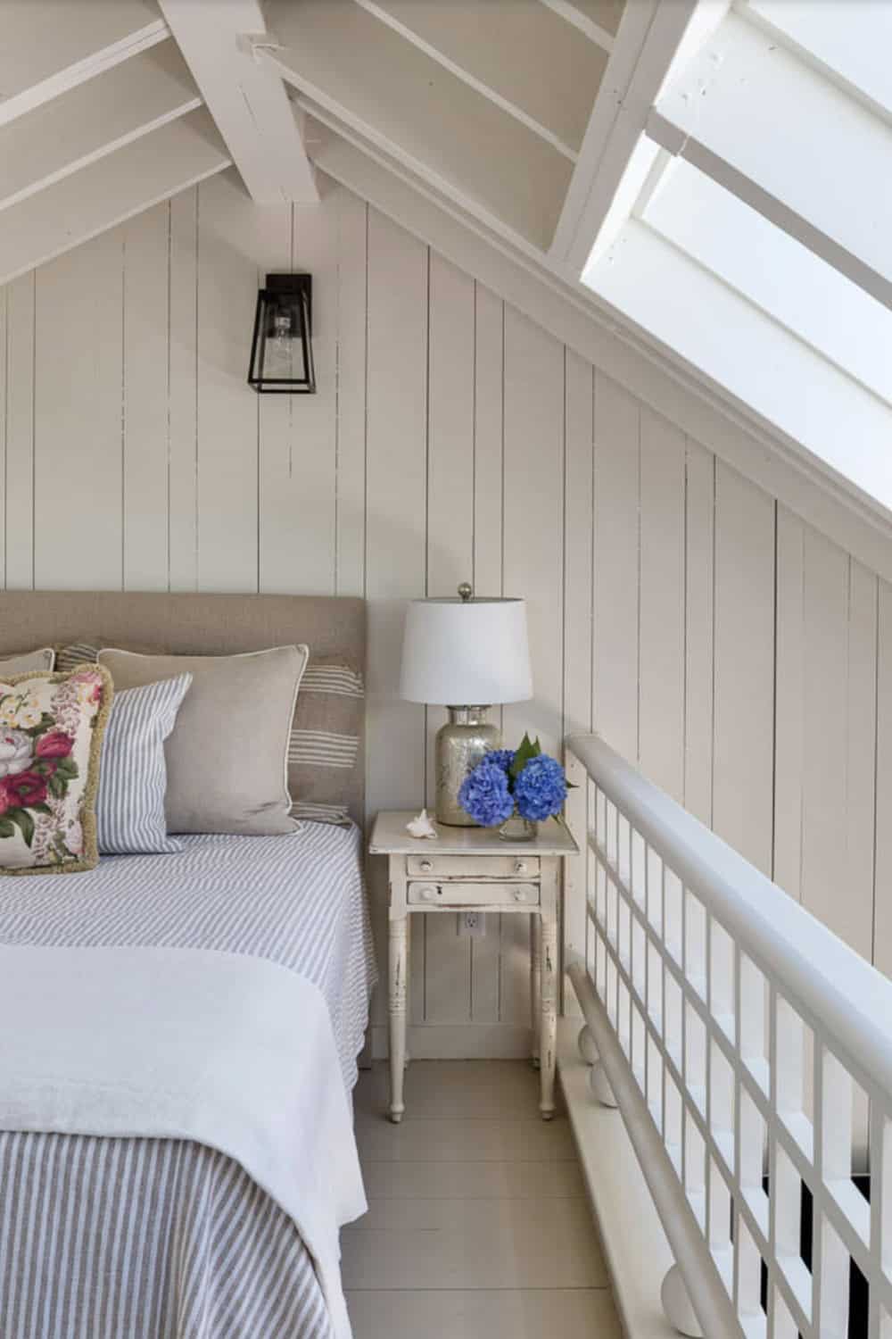 Cozy loft bedroom with sloped ceiling, ticking stripe bedding, floral pillows, and skylight