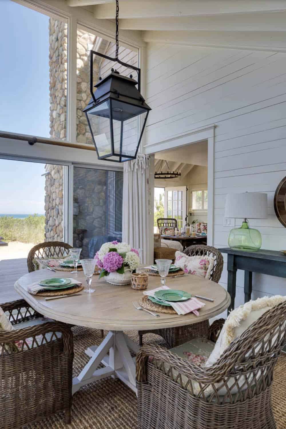 Covered porch dining area with round wood table, wicker chairs, black lantern pendant, and ocean views