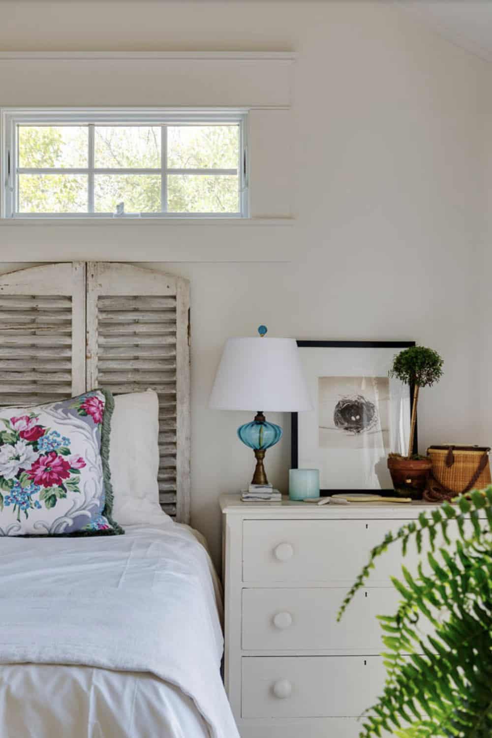 Beach cottage bedroom detail with vintage shutter headboard, floral pillow, blue glass lamp, and white dresser