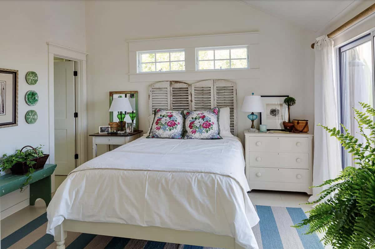 Bright cottage bedroom with vintage shutter headboard, floral pillows, striped rug, and sliding glass door