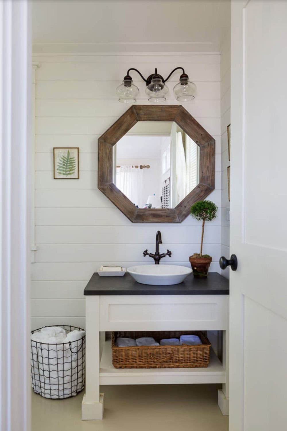 Cottage bathroom with octagonal wood mirror, vessel sink, dark countertop, and glass globe vanity lights