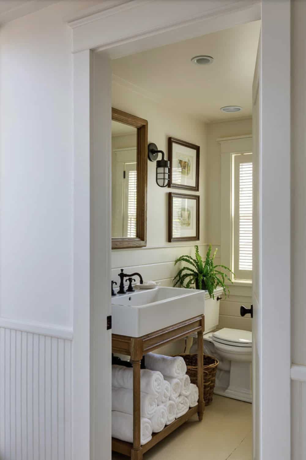 Cottage bathroom with wood-framed mirror, farmhouse sink on open vanity, cage sconce, and framed botanical art