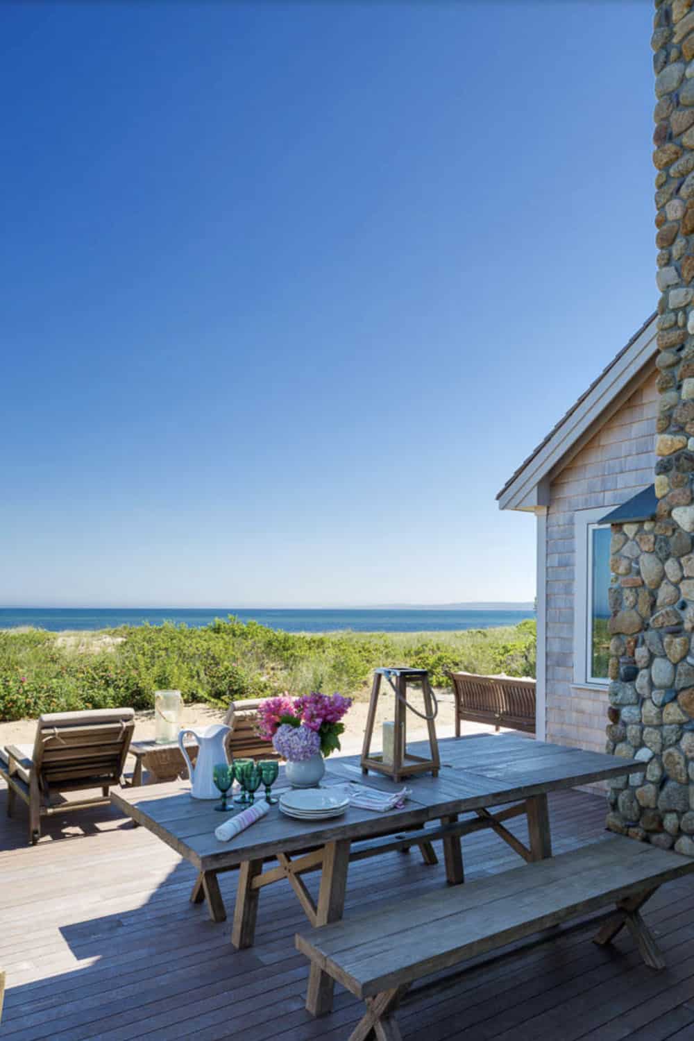 Oceanfront deck with wood picnic table, hydrangea centerpiece, green glassware, and river rock chimney