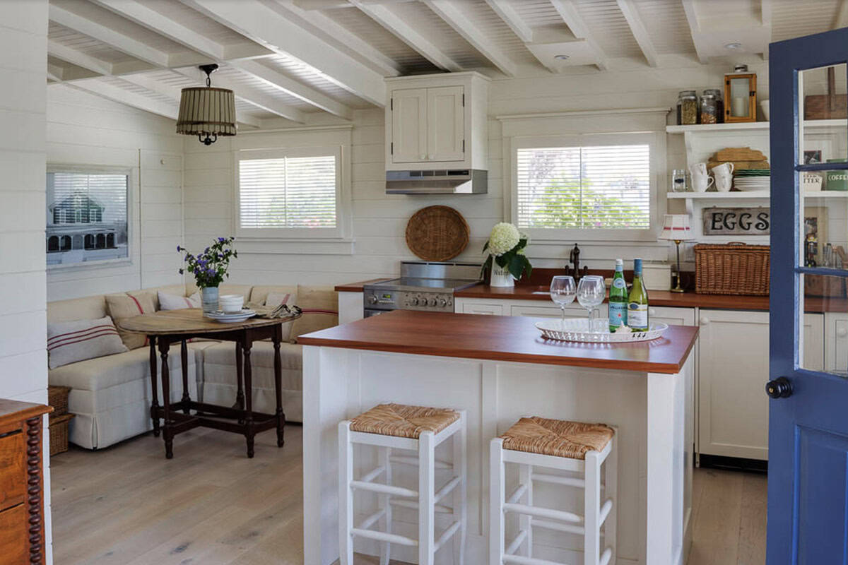 Cottage kitchen with white island, wood countertops, rush bar stools, open shelving, and breakfast nook