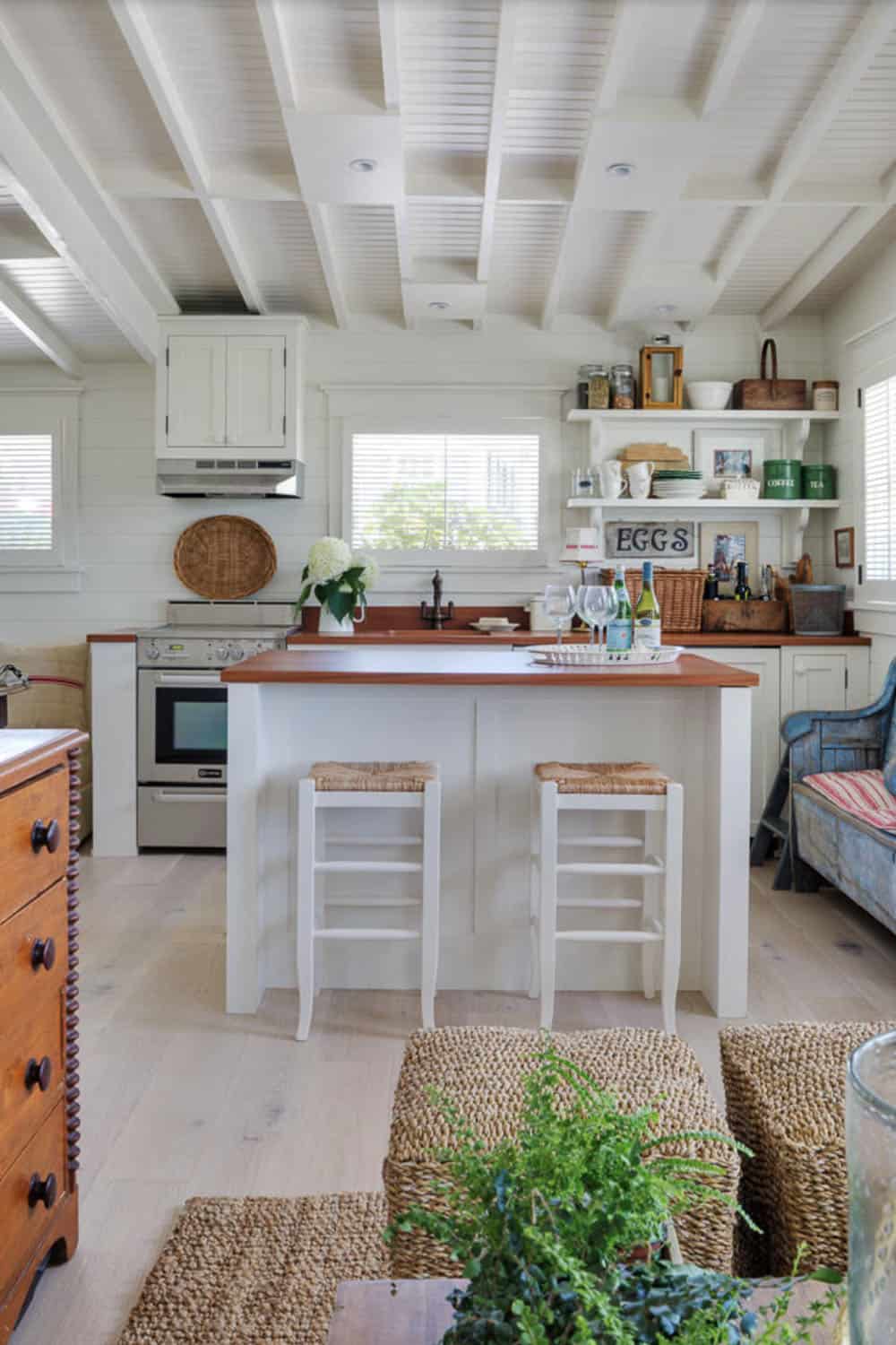 Cottage kitchen with white cabinets, wood countertops, open shelving, exposed beams, and bar island